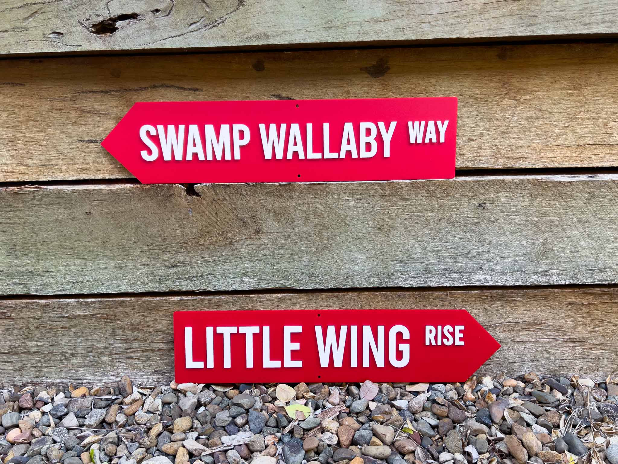 Two red and white street style signs that say 'SWAMP WALLABY WAY' & 'LITTLE WING RISE'.